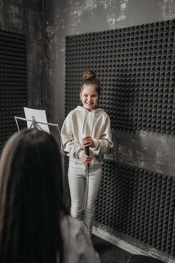 A young girl sings in a music studio, holding a microphone confidently.